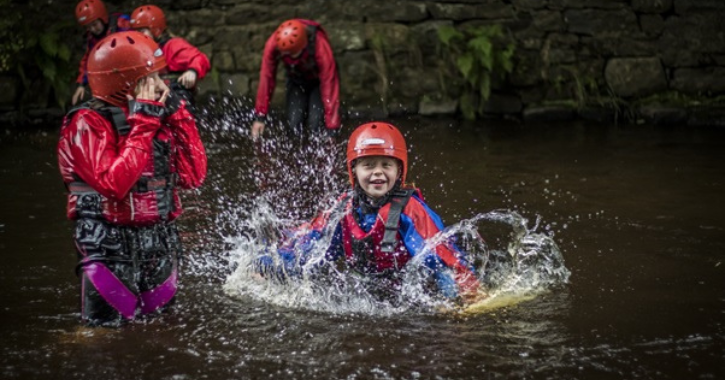 Children in wet suits and helmets splashing in water at Weardale Adventure Centre.